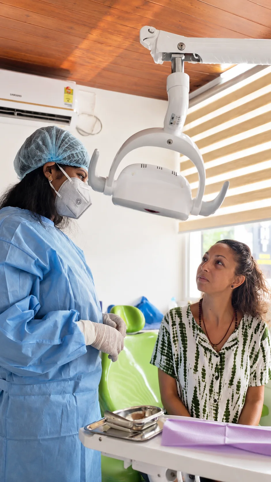 A gowned and masked clinician talking with a patient beside the treatment chair before surgery
