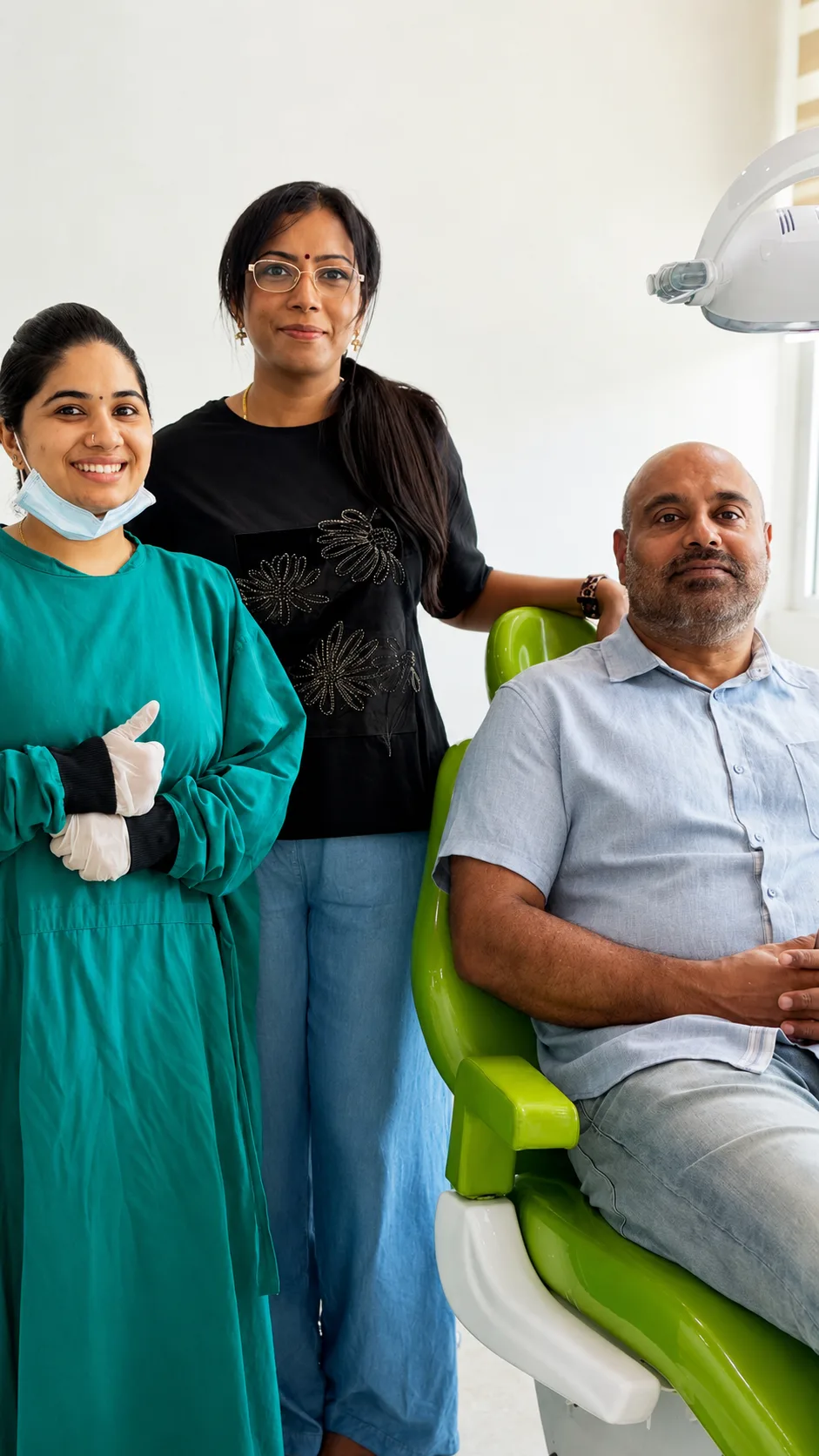 Two clinicians standing beside a patient seated in the green treatment chair, one giving a thumbs up