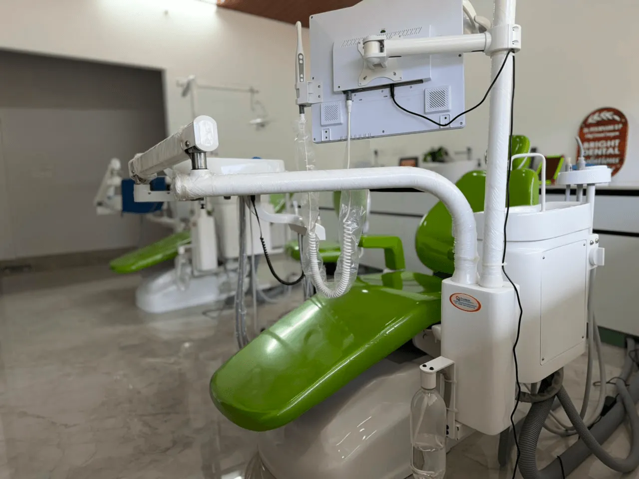 A green dental chair with its overhead light and instrument tray prepared for a patient