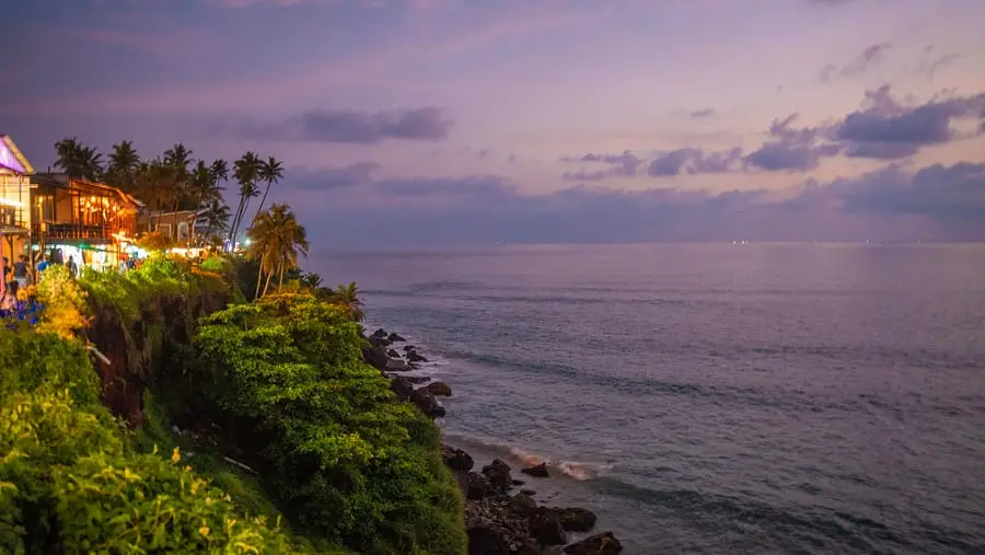 The Varkala cliff at dusk, the clifftop cafés lit against a violet sky