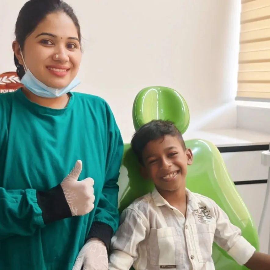 A boy grinning in the dental chair while his dentist gives a thumbs-up