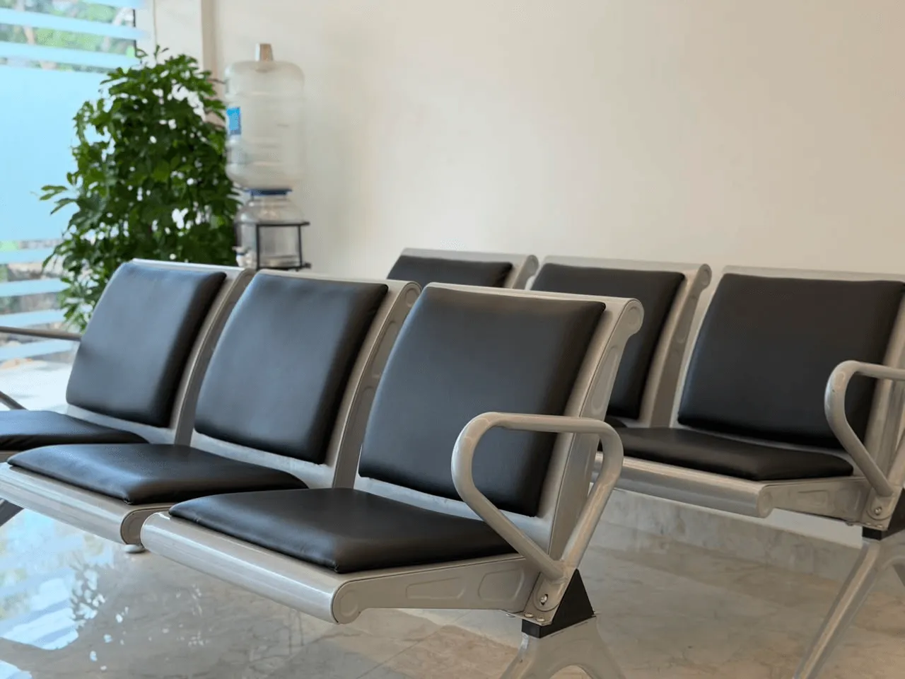 A row of cushioned steel seats in the clinic waiting area beside a potted plant